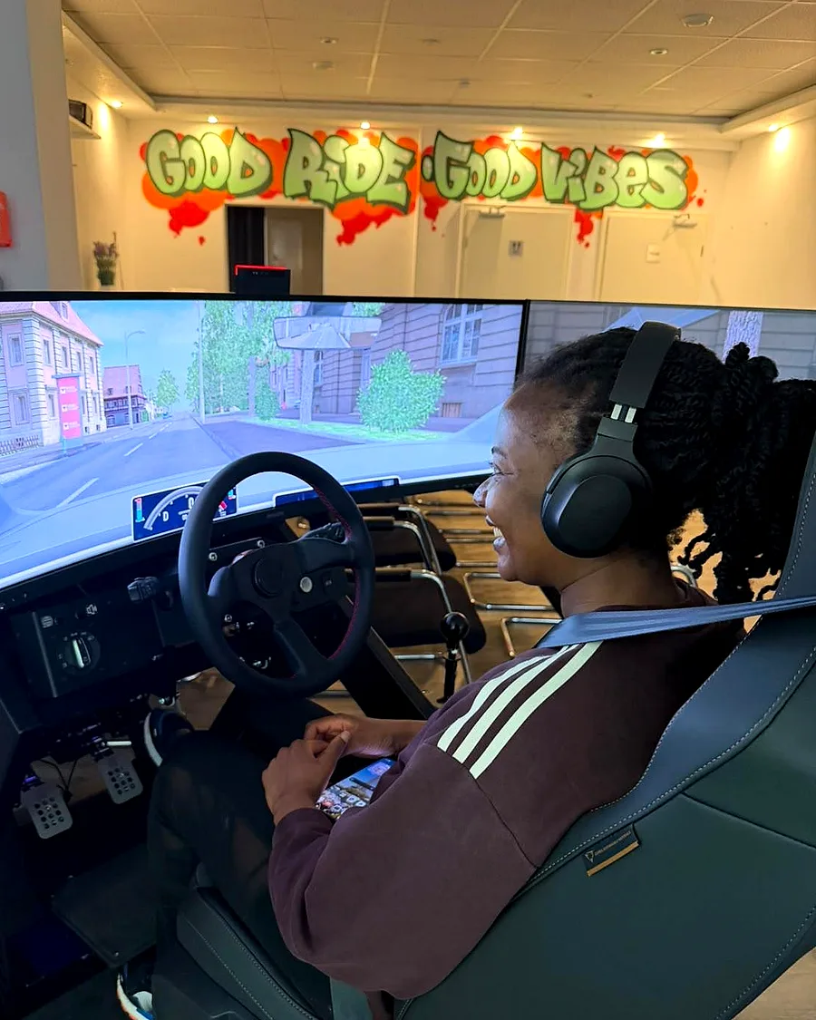 Fahrschülerin mit Kopfhörern lacht am Fahrsimulator der Fahrschule Graf – Lenkrad, Pedale und große Bildschirme